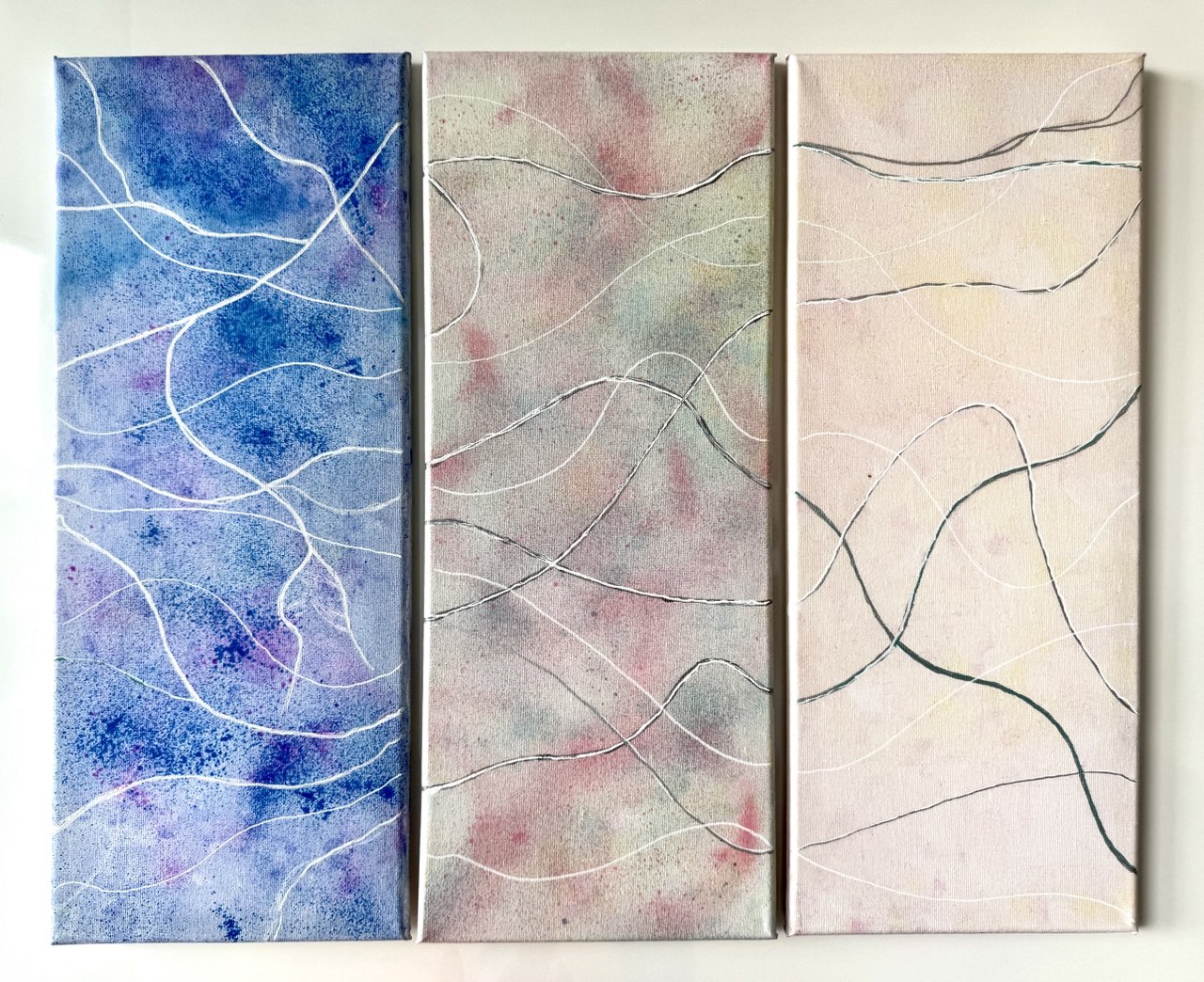Three narrow canvases: blue-to-lilac, soft gray-pink, and pale sand tones, crossed by fine flowing lines.